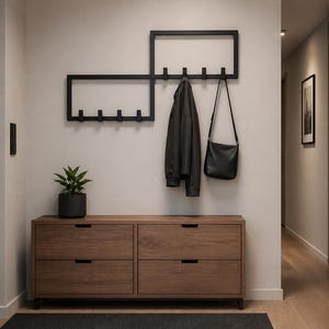 Op de afbeelding: Een moderne entree met een houten dressoir, een zwarte kapstok en een zwarte leren tas. Een zwarte jas hangt aan de kapstok. Een plant in een pot staat op het dressoir. De muren zijn neutraal.
