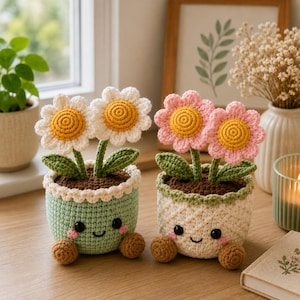 May include: Two crocheted potted flowers with smiling faces. The left pot is light green with white daisies, and the right pot is cream with pink flowers. Both have brown soil, green stems, dark eyes, and small brown feet on a wooden surface.