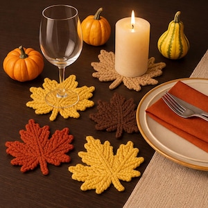 Puede incluir: Una mesa con decoración otoñal, incluyendo una vela encendida, calabazas y posavasos con forma de hoja en tonos amarillos, naranjas y marrones. Una copa de vino y un plato con servilleta y tenedor completan la escena, creando un ambiente cálido.