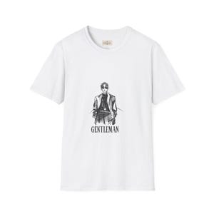May include: White t-shirt featuring a black and white illustration of a person in a suit and sunglasses. The word "GENTLEMAN" is printed in black below the illustration. The shirt has a crew neck and short sleeves.