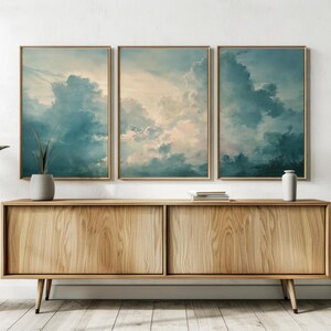 May include: Three framed prints showcasing a cloudy sky in teal, blue, and cream tones. They are mounted above a wooden cabinet with a natural finish. Decorative plants and vases enhance the room's decor.