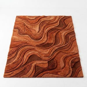 May include: A rectangular rug with a textured, wavy pattern in shades of brown and orange. The rug's design features a layered effect, creating a sense of depth and dimension. The colour palette ranges from light tan to deep reddish-brown.