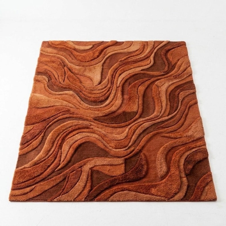 May include: A rectangular rug with a textured, wavy pattern in shades of brown and orange. The rug's design features a layered effect, creating a sense of depth and dimension. The colour palette ranges from light tan to deep reddish-brown.