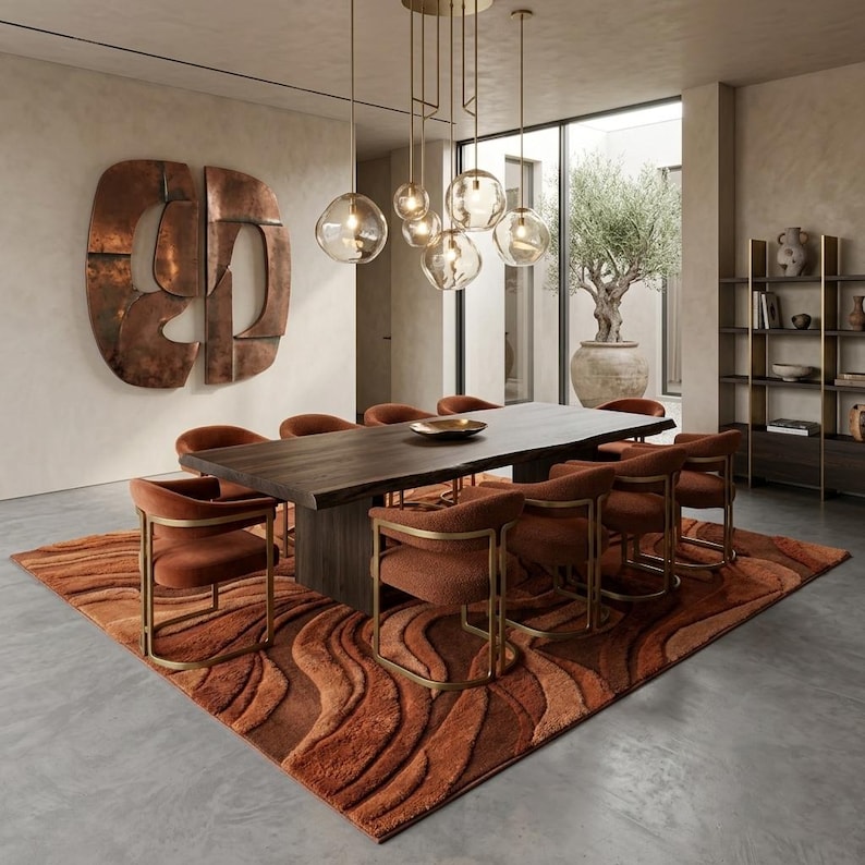 May include: A contemporary dining room with a dark wood table and eight rust-coloured chairs. A large, patterned rug in shades of orange and brown is under the table. Globe pendant lights hang above the table, and a large copper wall sculpture is on the wall.