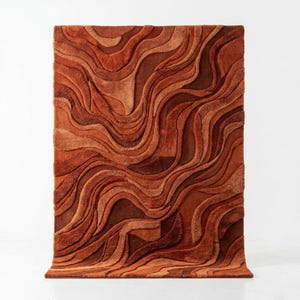 May include: A rectangular rug with a textured surface, in shades of orange and brown. The rug's design features a wavy, layered pattern, creating a three-dimensional effect. The colour palette ranges from light orange to deep brown, adding depth to the floor covering.