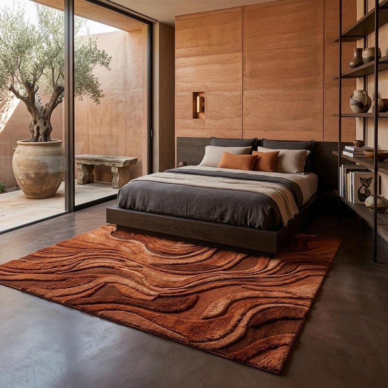 May include: A contemporary bedroom with a dark bed and neutral-toned bedding. A rust-coloured rug with a wave design lies on the floor. The room has a neutral colour scheme and natural light. The rug's pattern creates a sense of movement.