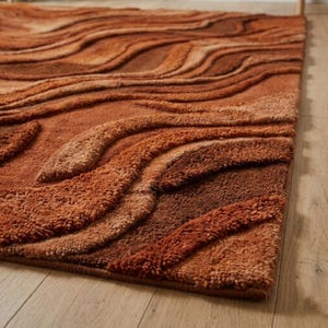 May include: A close-up of a brown rug with a textured, wavy pattern. The rug features varying shades of brown, creating a layered, three-dimensional effect. The rug's design resembles flowing waves or layered terrain, adding visual interest to the floor covering.