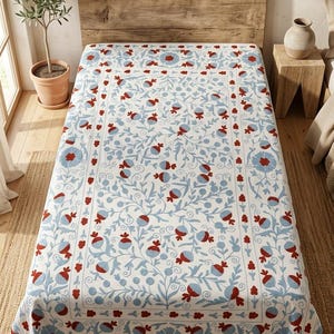 May include: A white bedspread with a floral pattern in blue and red. The design features stylized flowers and vines, creating a decorative and elegant look. The bedspread is placed on a bed with a wooden headboard.