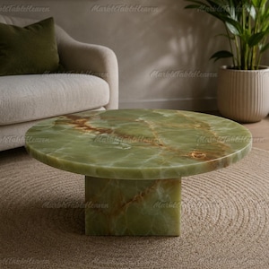 May include: A round coffee table crafted from green onyx stone featuring natural brown veining throughout the surface. The table has a smooth, polished circular top supported by a solid, square-shaped pedestal base made of the same green onyx material.