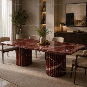 May include: A rectangular dining table featuring a polished deep red marble top with white veining, supported by two cylindrical, fluted bases crafted from the same matching red marble. The table is surrounded by four beige upholstered chairs.