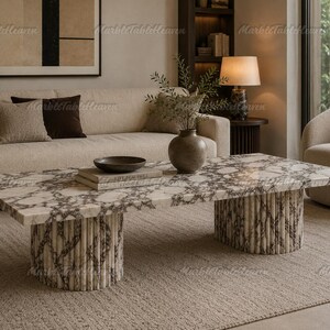 May include: A rectangular coffee table featuring a white marble top with dark grey veining and two cylindrical, fluted marble bases. The table surface is smooth and polished, showcasing a natural stone pattern throughout the entire structure.