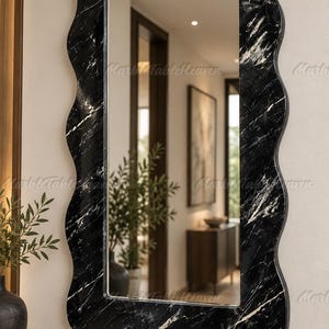 May include: A rectangular wall mirror featuring a wavy, scalloped frame made of black marble with prominent white veining. The reflective glass surface is clear and smooth, set within the dark, polished stone border that has a distinct undulating edge.
