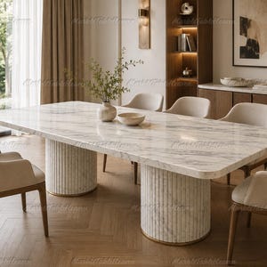 Puede incluir: Una mesa de comedor rectangular con una superficie de mármol blanco con vetas grises. La mesa se apoya sobre dos bases cilíndricas con textura estriada vertical y un borde de metal dorado en la parte inferior, rodeada por seis sillas tapizadas.