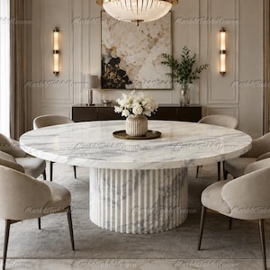 May include: A large round dining table with a white marble top featuring grey veining and a cylindrical fluted marble base. The table is surrounded by six upholstered beige chairs with dark metal legs and holds a central vase of white flowers.