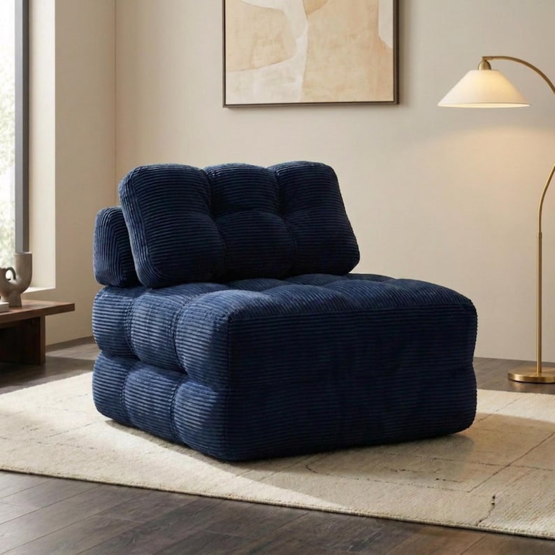 May include: A navy blue corduroy modular sofa with a tufted design. The sofa has a low profile and a boxy shape, with a separate backrest and armrest. It sits on a light-colored rug in a well-lit room.