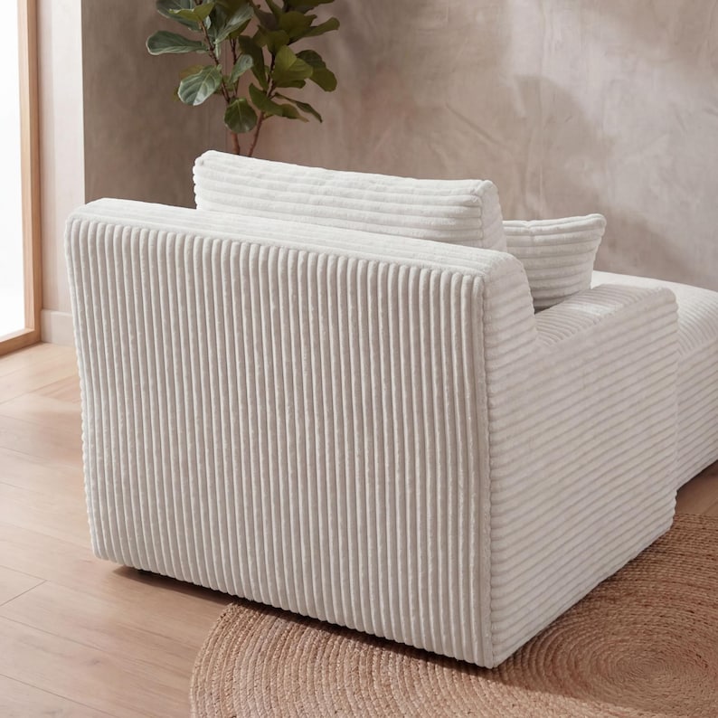 May include: A cream-colored corduroy armchair with a matching pillow. The chair has a ribbed texture and a rounded back. The chair is placed on a round, woven rug.