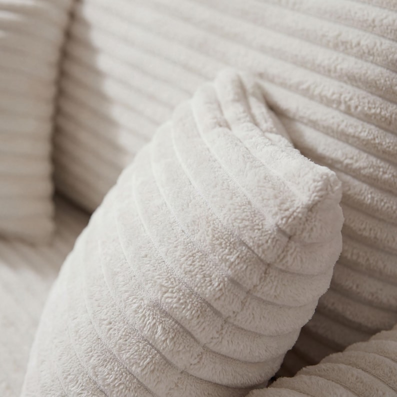 May include: Close-up of a soft, white corduroy pillow. The fabric has a ribbed texture, with the ridges running diagonally across the pillow's surface. The pillow appears plush and comfortable, suggesting a cozy home decor item.