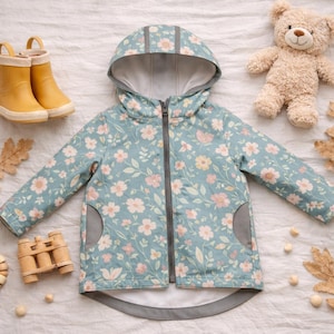 Puede incluir: Chaqueta azul claro con estampado floral, capucha y cierre de cremallera. La chaqueta tiene forro y bolsillos grises. Botas de agua amarillas y un oso de peluche también están en la imagen.