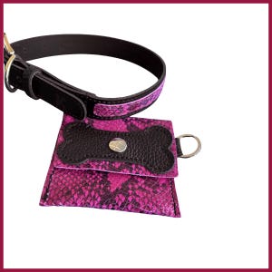 Può includere: Un collare nero per cani con un motivo a pelle di serpente rosa e una custodia abbinata. La custodia ha una patta a forma di osso e una chiusura in metallo argentato. Sfondo bianco.