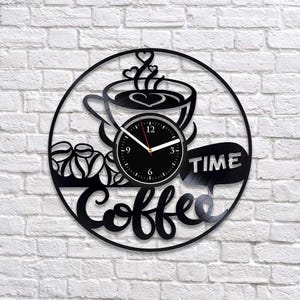 Pode incluir: Um relógio de parede circular preto feito de um disco de vinil com um design recortado de uma xícara de café com vapor em forma de coração, grãos de café e o texto Coffee TIME. O mostrador é preto com números e ponteiros brancos.