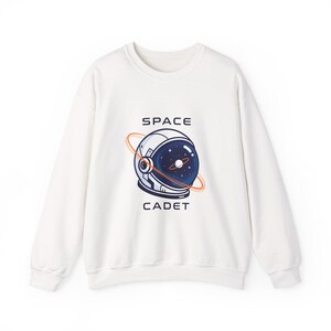 Könnte beinhalten: Weißes Sweatshirt mit Rundhalsausschnitt und einer Grafik eines Weltraumhelms mit den Worten "SPACE CADET" in Marineblau. Das Helmdesign zeigt einen Sternenhimmel und eine orangefarbene Umlaufbahn.