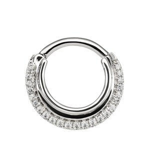 May include: A circular hinged segment ring made of polished silver-toned metal. The outer edge of the hoop is embellished with a single row of small, clear, round-cut stones that span approximately two-thirds of the ring's circumference.