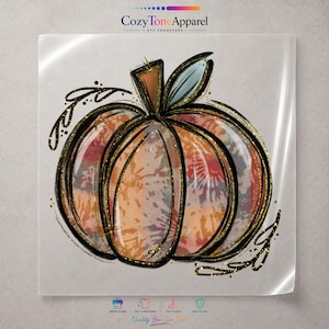 May include: A pumpkin graphic design featuring a tie-dye pattern in shades of orange, blue, and white. The pumpkin is outlined in bold black lines with gold glitter accents and decorative swirls. The text CozyToneApparel DTF TRANSFERS is visible.