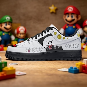 May include: White and black sneaker featuring a cartoon Boo design with the word "BOO!" and other Super Mario Bros. graphics. The shoe has a black sole and laces, with a black swoosh. The shoe is on a wooden surface.