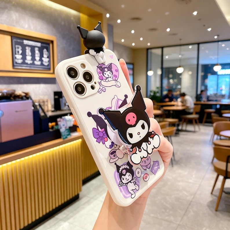 May include: White phone case with a cartoon character design. The case features a black and white character with a pink face and a 3D figure on top. Purple and pink accents are visible.