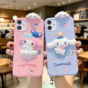 Può includere: Due custodie per telefono, una rosa e una blu, ciascuna con un design di personaggi dei cartoni animati in 3D. La custodia rosa ha un tema My Melody, mentre quella blu presenta Cinnamoroll. Entrambe le custodie hanno un design a nuvola e cuore.