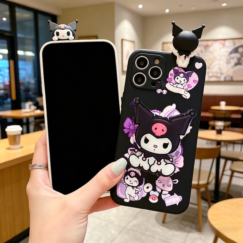 May include: Black and white phone case with a cartoon character design. The case features a 3D figure at the top and a detailed graphic of the character with purple accents. The phone case is held next to a blank phone.