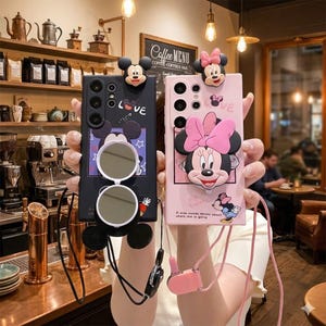Può includere: Custodie per telefono nere e rosa con disegni di Topolino e Minnie Mouse. La custodia nera ha occhiali da sole e la parola "LOVE". La custodia rosa ha una citazione e un fiocco di Minnie Mouse.