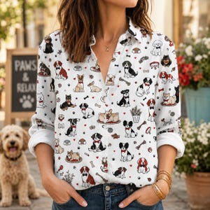 May include: A white long-sleeve button-down shirt featuring an all-over print of various dog breeds, small red hearts, bones, and paw prints. The shirt has a classic collar, a front button placket, and cuffs rolled up to the mid-forearm.