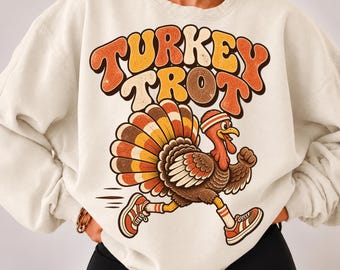 May include: A cream-colored crewneck sweatshirt featuring a graphic of a turkey wearing a headband and sneakers. The text "TURKEY TROT" is printed above the turkey in large, bold, orange and yellow letters with a distressed texture.