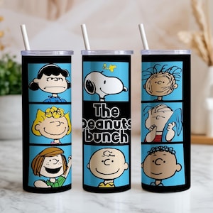 Puede incluir: Tres vasos cil&iacute;ndricos con tapas transparentes y pajitas blancas, con un dise&ntilde;o de c&oacute;mic en azul y negro. Los gr&aacute;ficos muestran varios personajes de Peanuts, incluidos Snoopy, Charlie Brown y Lucy, con el texto The peanuts bunch.