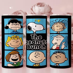 Puede incluir: Un vaso cil&iacute;ndrico con un estampado gr&aacute;fico en azul y negro de los personajes de Peanuts, incluyendo a Snoopy, Woodstock, Charlie Brown, Lucy, Sally, Linus y Franklin, con el texto The Peanuts bunch impreso en negro en el panel central.