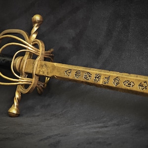 May include: A golden sword with an ornate hilt and a black handle. The blade is engraved with symbols. The sword has a complex guard design with spiral accents. The overall aesthetic suggests a historical or fantasy theme.