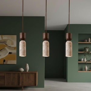 Puede incluir: Tres lámparas colgantes cilíndricas que cuelgan del techo. Cada luminaria presenta una tapa superior de madera marrón oscuro conectada a una base texturizada de piedra beige claro con detalles moteados en gris y negro, emitiendo luz suave.