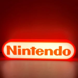 May include: An illuminated sign displaying the word "Nintendo" in orange. The sign has a white background and an orange border. The background is a gradient of red.