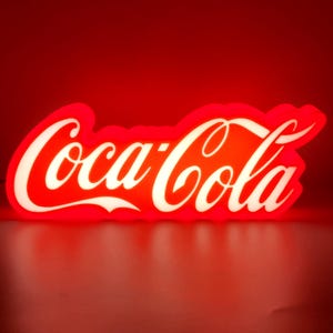 May include: A red and white Coca-Cola neon sign. The sign displays the Coca-Cola logo in white script against a red background. The illuminated sign creates a bright and striking visual effect.