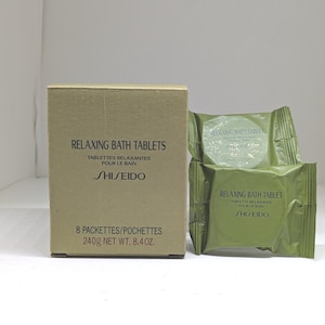 Può includere: Una scatola di cartone color marrone chiaro con l'etichetta Relaxing Bath Tablets Shiseido 8 Packettes 240g accanto a due involucri individuali di compresse da bagno verde oliva con lo stesso testo e marchio stampati in nero sul davanti.