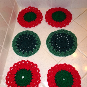 May include: Six handmade crochet coasters. Two are red with a green center and scalloped edges. Two are green with a white center. The remaining two are red with a green center and scalloped edges. The coasters are circular.