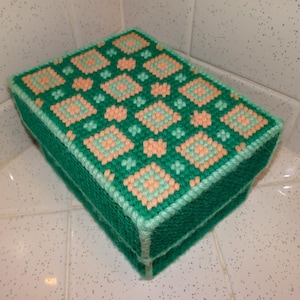 Puede incluir: Una caja rectangular hecha a mano, verde con un patrón repetido de diamantes melocotón y verde claro en la tapa. Los bordes están bordeados con un borde verde claro.
