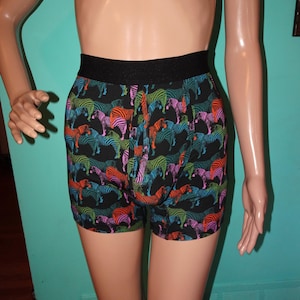 May include: Black boxer shorts with a colorful zebra print. The zebras feature stripes in shades of orange, pink, blue, and green. The waistband is black. The shorts are made of a soft, comfortable material.
