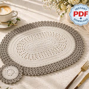Può includere: Un runner ovale all'uncinetto bianco sporco e grigio con un sottobicchiere abbinato. Il runner presenta un design traforato dettagliato e un bordo smerlato. Sono visibili anche una tazza di caffè, un cucchiaio e posate dorate.