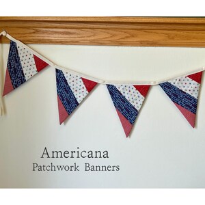May include: A patriotic Americana patchwork banner with red, white, and blue triangle flags. The flags are strung together with a white ribbon. The banner is hanging against a white wall. Text on the wall reads "Americana Patchwork Banners."
