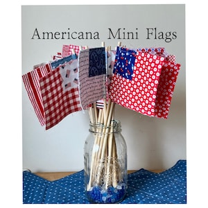 May include: Americana Mini Flags. A collection of small fabric flags in red, white, and blue patterns, including stripes, polka dots, and stars. The flags are attached to wooden dowels and displayed in a clear glass jar. The text "Americana Mini Flags" is at the top.
