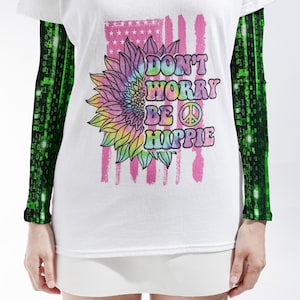 May include: A white short-sleeve t-shirt with long black sleeves featuring a green digital binary code pattern. The front displays a tie-dye sunflower, a pink American flag graphic, and the text DON'T WORRY BE HIPPIE with a peace sign symbol.