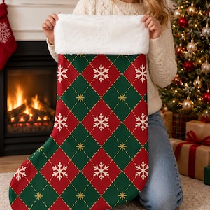 Puede incluir: Un calcetín navideño con un patrón de rombos en rojo y verde oscuro, decorado con motivos de copos de nieve blancos y pequeñas estrellas amarillas. El calcetín tiene un borde grueso de piel sintética blanca y una silueta clásica de bota.
