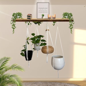 May include: A wooden shelf with hanging planters and greenery. The shelf holds small books, candles, and a framed print that reads "Simply Korded HANDMADE". Below, four planters of varying shapes and colours hang from macrame hangers.